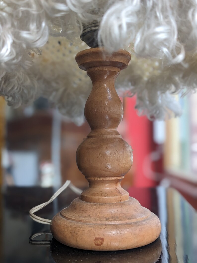 Op de afbeelding: Een houten lampenvoet met een witte, pluche lampenkap. De voet heeft een bolle vorm met een afgeronde bovenkant en een brede basis.