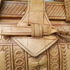 Puede incluir: Un bolso de cuero marr&oacute;n con intrincados dise&ntilde;os en relieve y una correa trenzada. El bolso tiene un cierre de solapa con una hebilla.