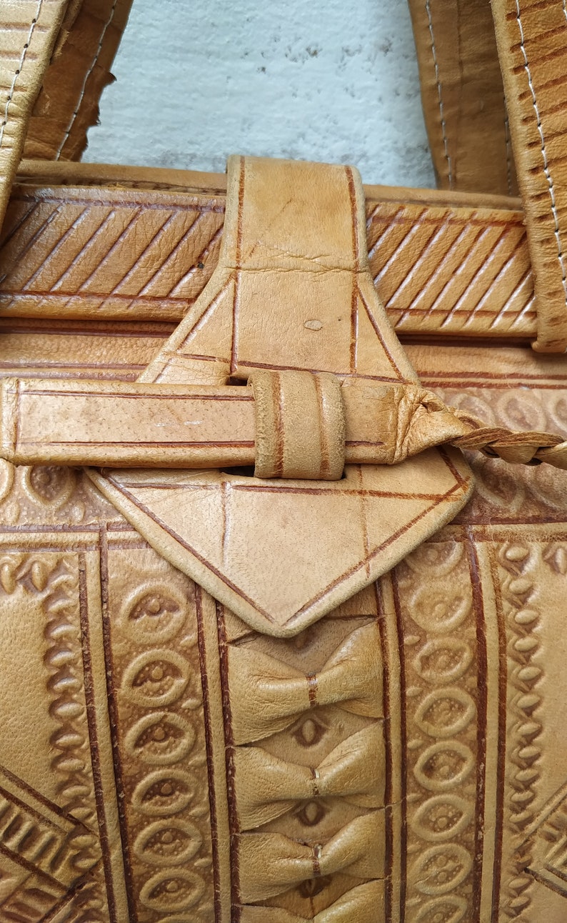 Puede incluir: Un bolso de cuero marr&oacute;n con intrincados dise&ntilde;os en relieve y una correa trenzada. El bolso tiene un cierre de solapa con una hebilla.