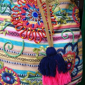 May include: A colorful striped drawstring bag with embroidered flowers and beads. The bag has a brown leather strap and a pink and blue tassel.