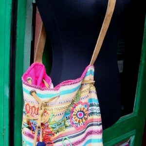 May include: A colorful striped and embroidered tote bag with pink, blue, and yellow accents. The bag has a brown leather strap and a pink lining.