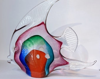 May include: A colorful glass sculpture of a fish with red, blue, green, and white accents. The fish is made of clear glass with a pink hue.