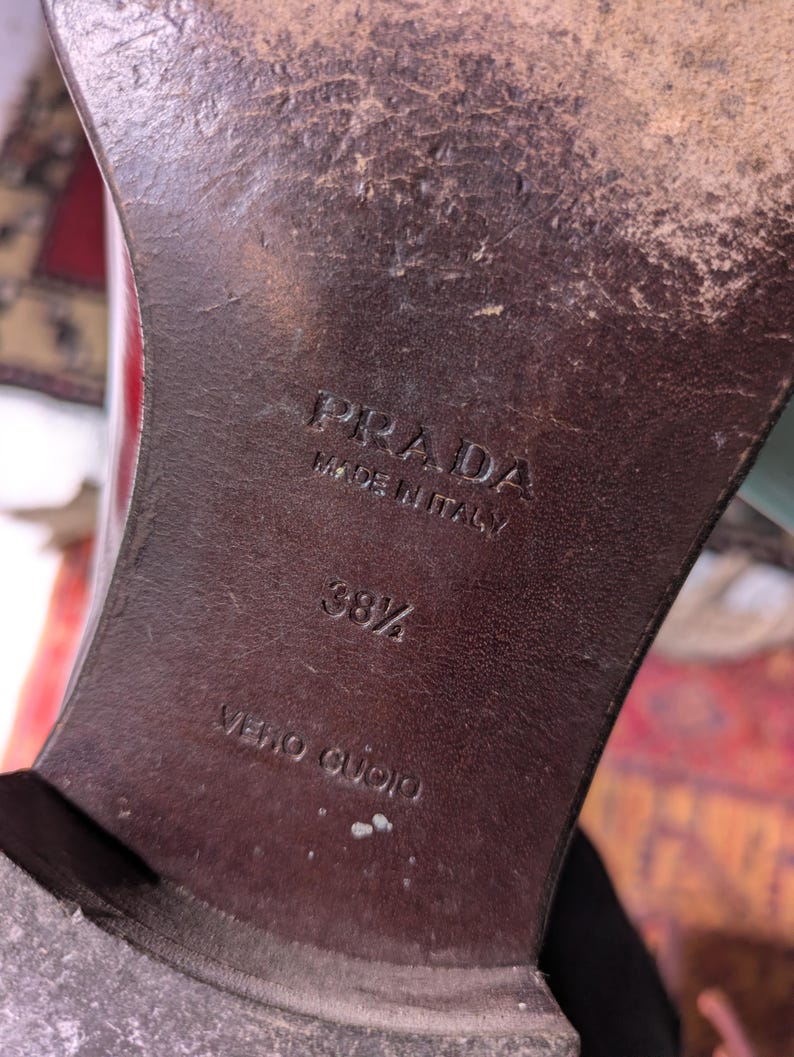May include: Close-up of a brown leather shoe sole with the embossed text "PRADA MADE IN ITALY". The size is marked as 38 1/2. The words "VERO CUOIO" are also visible.