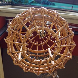 May include: A woven wicker lampshade with a circular design. The lampshade is made of natural brown wicker and has a spiral pattern.