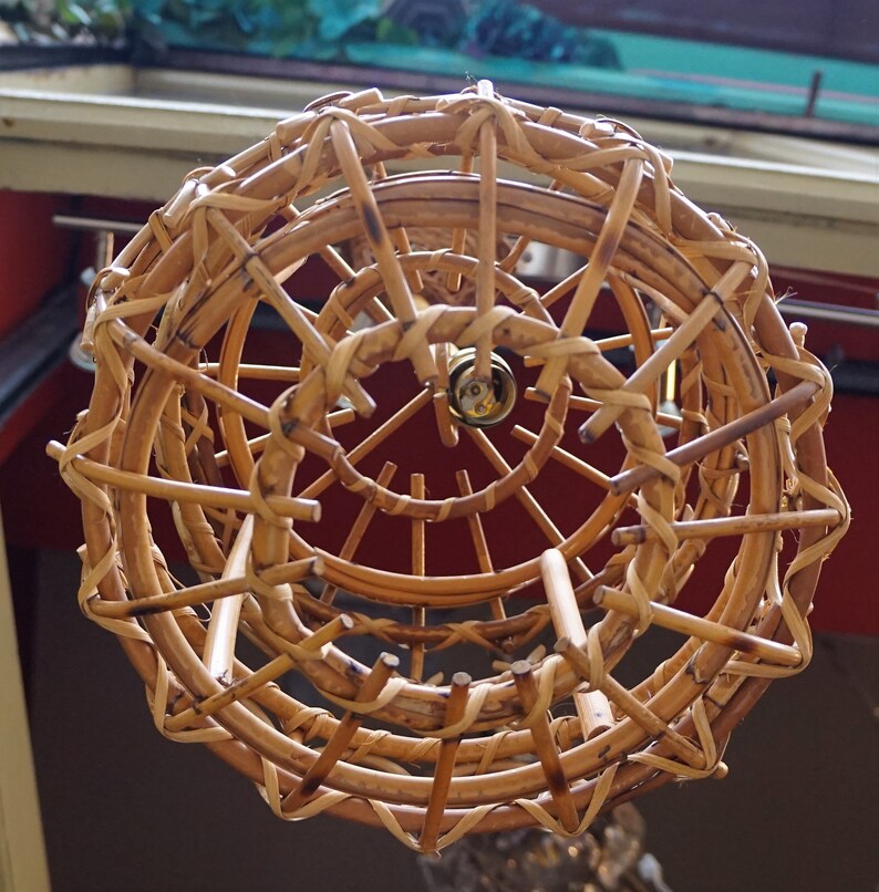 May include: A woven wicker lampshade with a circular design. The lampshade is made of natural brown wicker and has a spiral pattern.