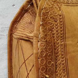 Puede incluir: Un bolso de cuero marr&oacute;n con intrincados detalles en relieve y costuras blancas. El bolso tiene un asa superior y un cierre de solapa.