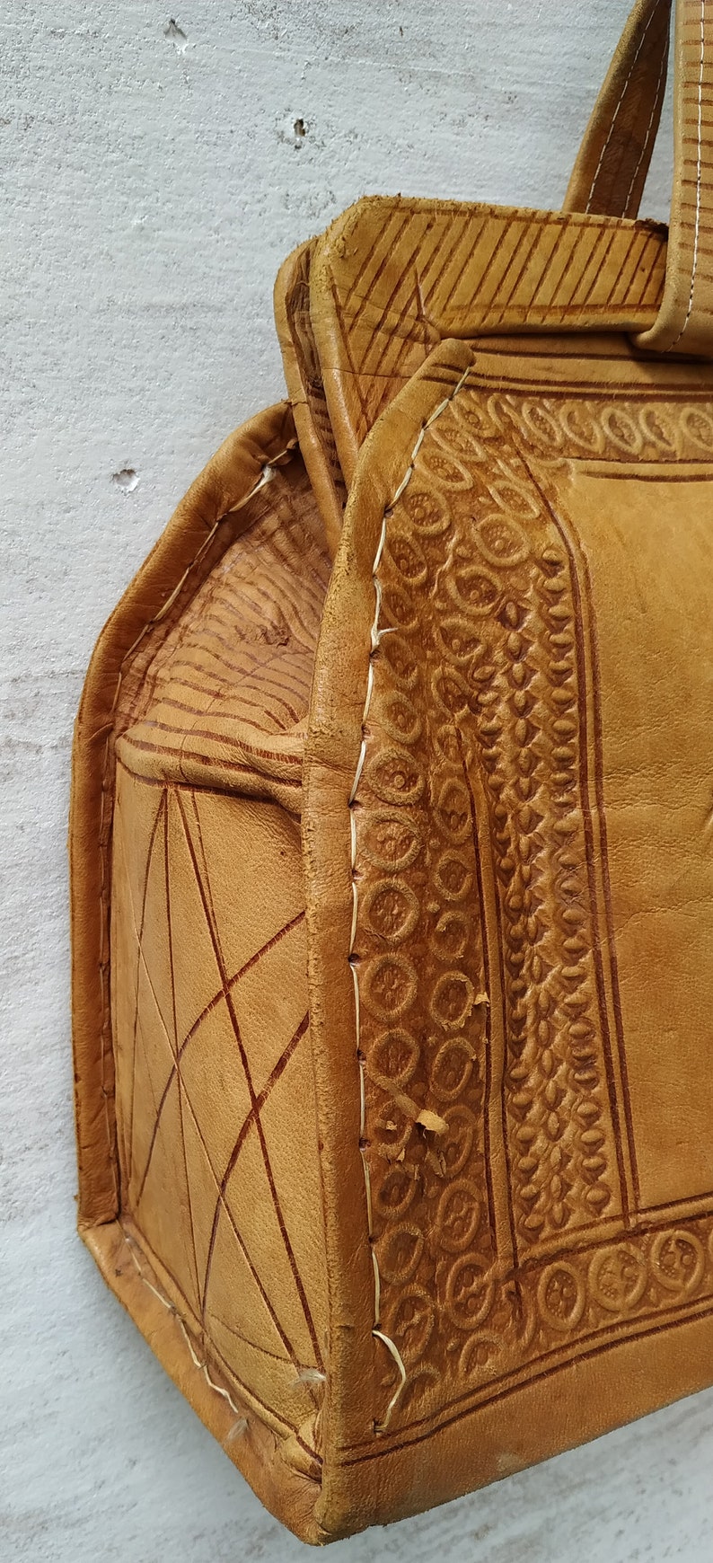 Puede incluir: Un bolso de cuero marr&oacute;n con intrincados detalles en relieve y costuras blancas. El bolso tiene un asa superior y un cierre de solapa.
