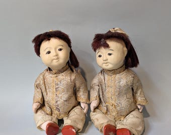 May include: Two vintage dolls with painted faces and brown hair wearing matching gold and white patterned outfits and red shoes.