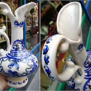 Peut inclure: Un pichet en céramique blanche avec des motifs floraux bleus et noirs. Le pichet a un corps large et rond et un bec verseur avec une poignée incurvée.