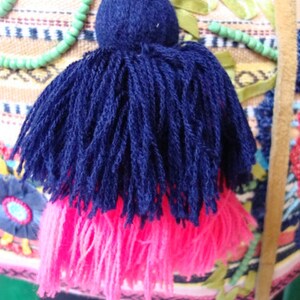 May include: A blue and pink tassel with a round, dark blue top. The tassel is made of soft, fluffy yarn and is attached to a string.