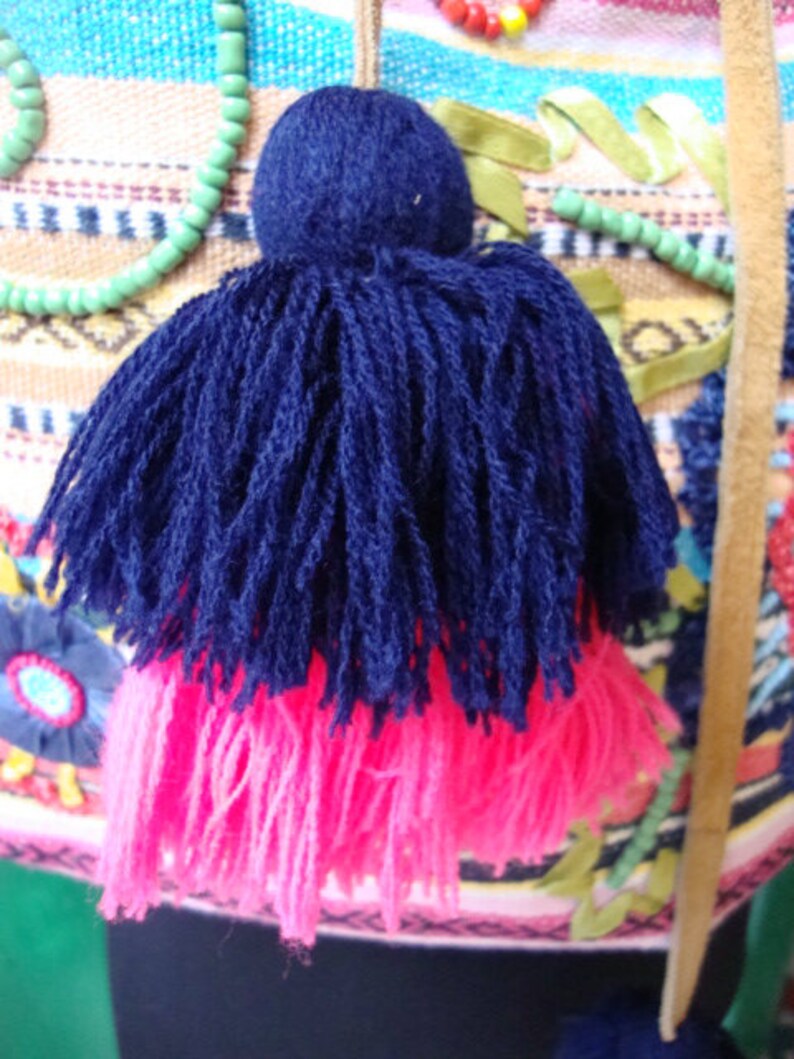 May include: A blue and pink tassel with a round, dark blue top. The tassel is made of soft, fluffy yarn and is attached to a string.