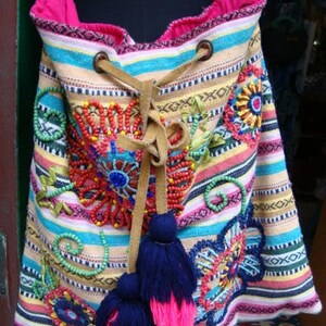 May include: A colorful striped fabric tote bag with embroidered flowers and beads. The bag has a drawstring closure and two tassels.