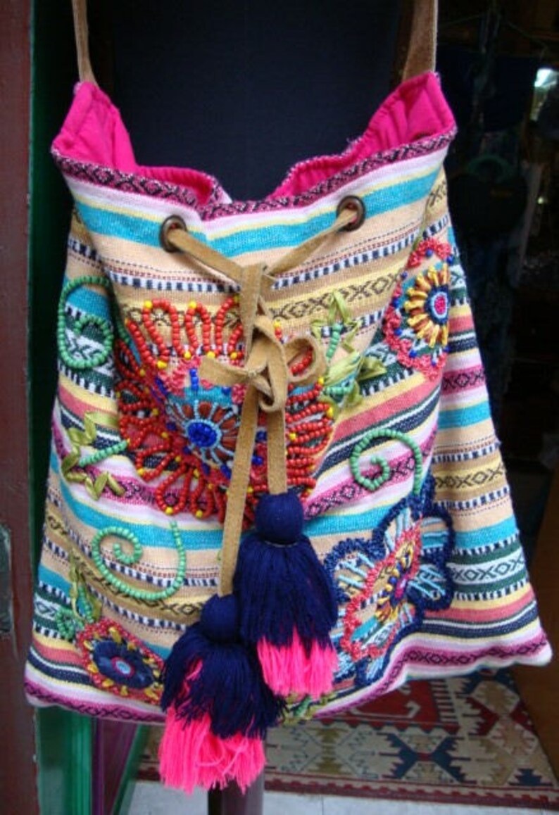 May include: A colorful striped fabric tote bag with embroidered flowers and beads. The bag has a drawstring closure and two tassels.