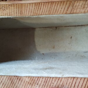 Puede incluir: El interior de una peque&ntilde;a caja rectangular con un exterior marr&oacute;n claro y un forro de tela blanco. La caja est&aacute; vac&iacute;a.