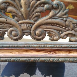 May include: A vintage ornate mirror frame with a gold and green finish. The frame has a detailed design with intricate carvings and a distressed look. The mirror is surrounded by a wooden frame with a brown and gold finish.