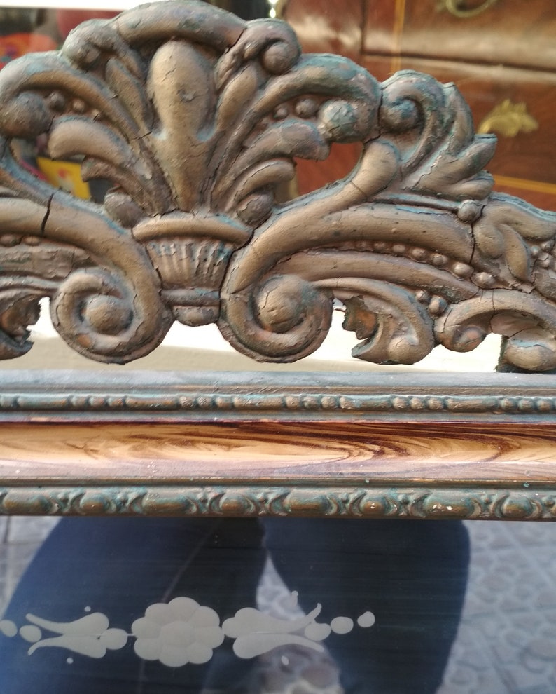 May include: A vintage ornate mirror frame with a gold and green finish. The frame has a detailed design with intricate carvings and a distressed look. The mirror is surrounded by a wooden frame with a brown and gold finish.