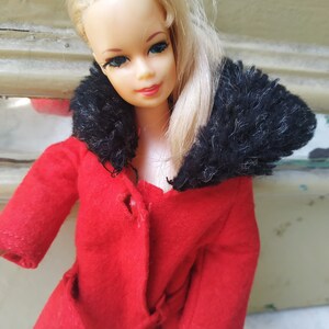 May include: A vintage Barbie doll wearing a red coat with a black fur collar. The doll has blonde hair and blue eyes.