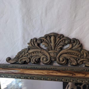 May include: A vintage mirror with a decorative, ornate, wooden frame. The frame is painted in a dark brown color with gold accents. The mirror has a rectangular shape and is surrounded by a detailed, carved design.