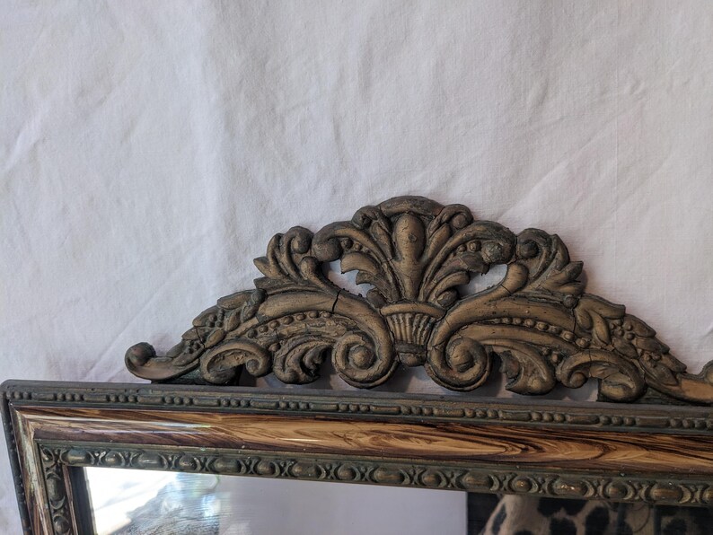 May include: A vintage mirror with a decorative, ornate, wooden frame. The frame is painted in a dark brown color with gold accents. The mirror has a rectangular shape and is surrounded by a detailed, carved design.