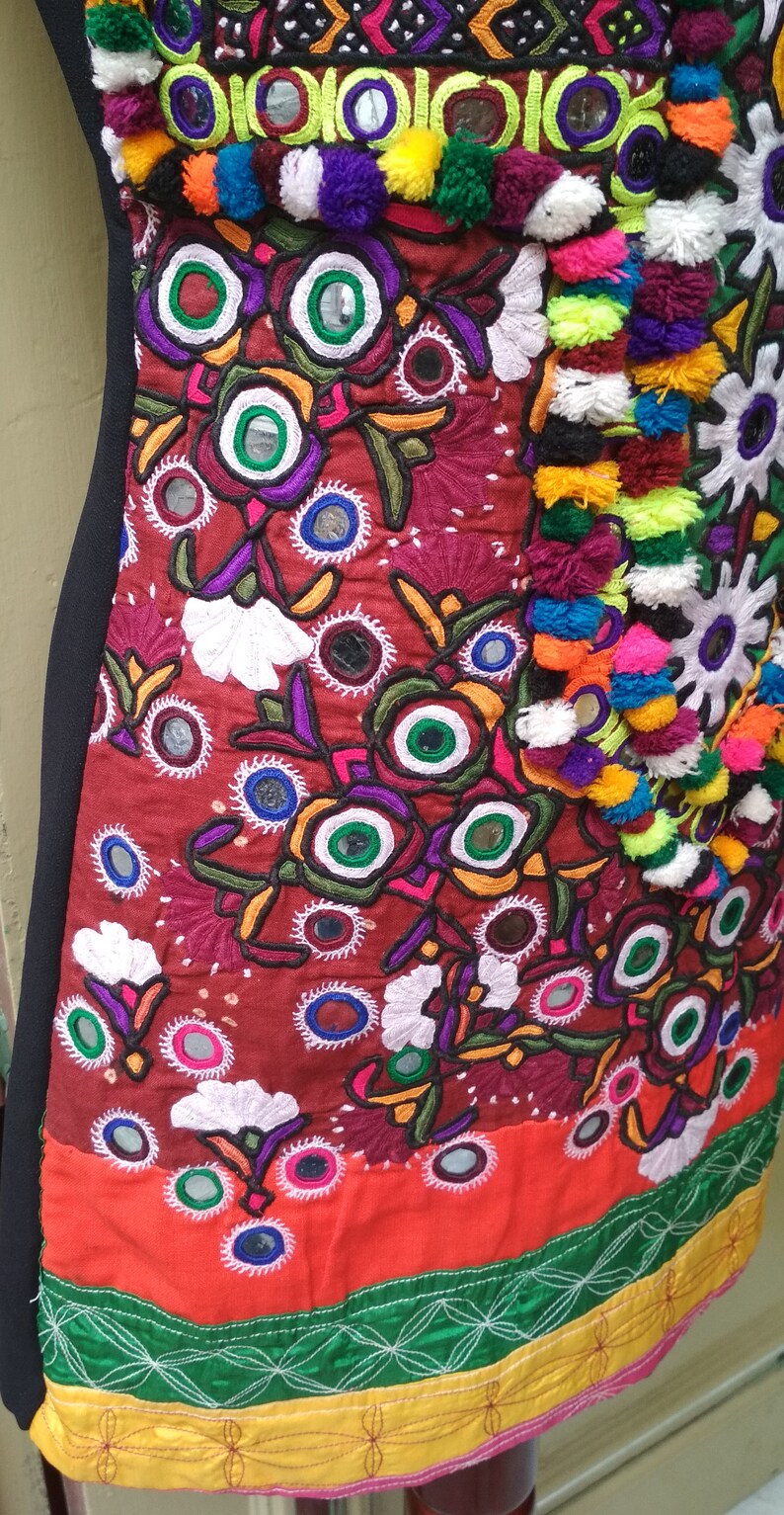 May include: A red, orange, green, and yellow embroidered fabric with colorful pom-poms and small round mirrors.