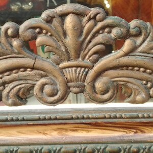 May include: A close-up of a decorative, ornate, gold-colored frame with intricate details. The frame is made of wood and has a distressed finish.