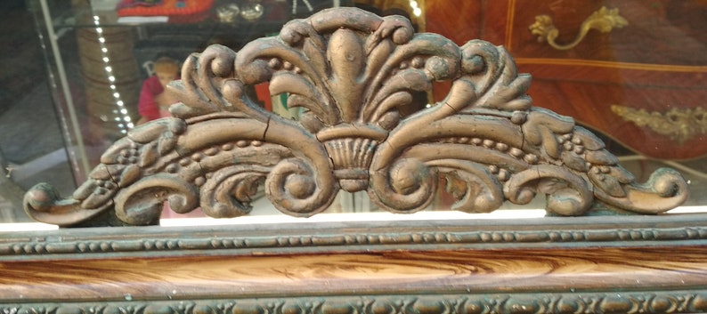 May include: A close-up of a decorative, ornate, gold-colored frame with intricate details. The frame is made of wood and has a distressed finish.