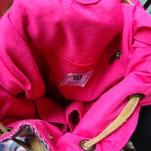 May include: Pink fabric backpack with a brown drawstring and a label that says "18".