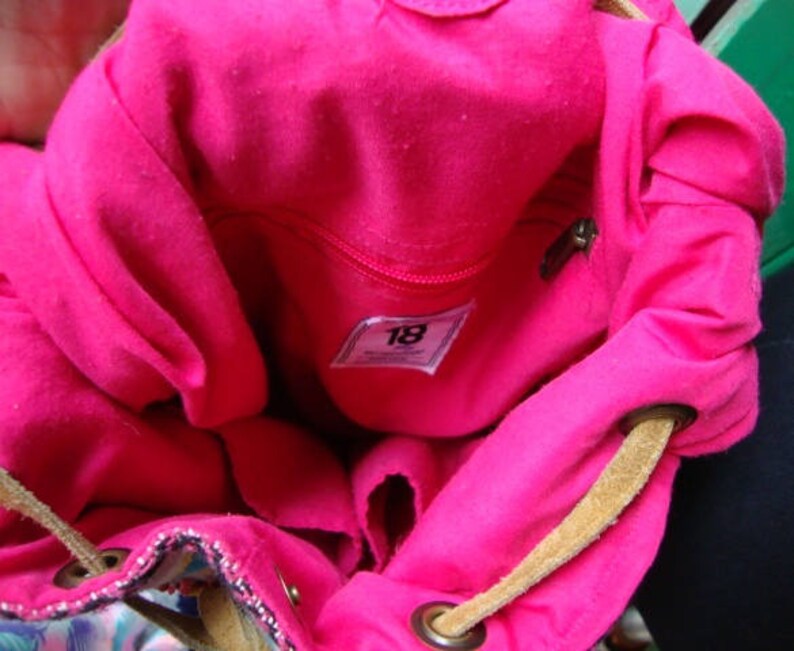 May include: Pink fabric backpack with a brown drawstring and a label that says "18".