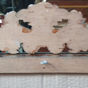 May include: The back of a wooden mirror frame with a decorative, ornate design. The frame is made of light wood with a natural finish. There is a small metal hook on the back of the frame.