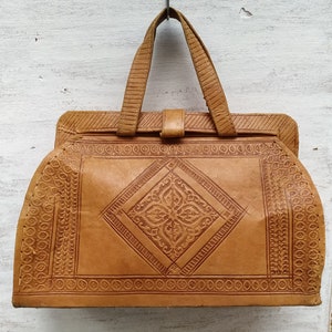 Puede incluir: Un bolso de mano de cuero marr&oacute;n con intrincados dise&ntilde;os en relieve. El bolso tiene un asa superior y un cierre de solapa.