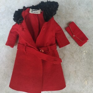 May include: A red coat with a black fur collar and a matching red clutch. The coat has a belt and a button closure. The label on the coat reads "Barbie by Mattel."