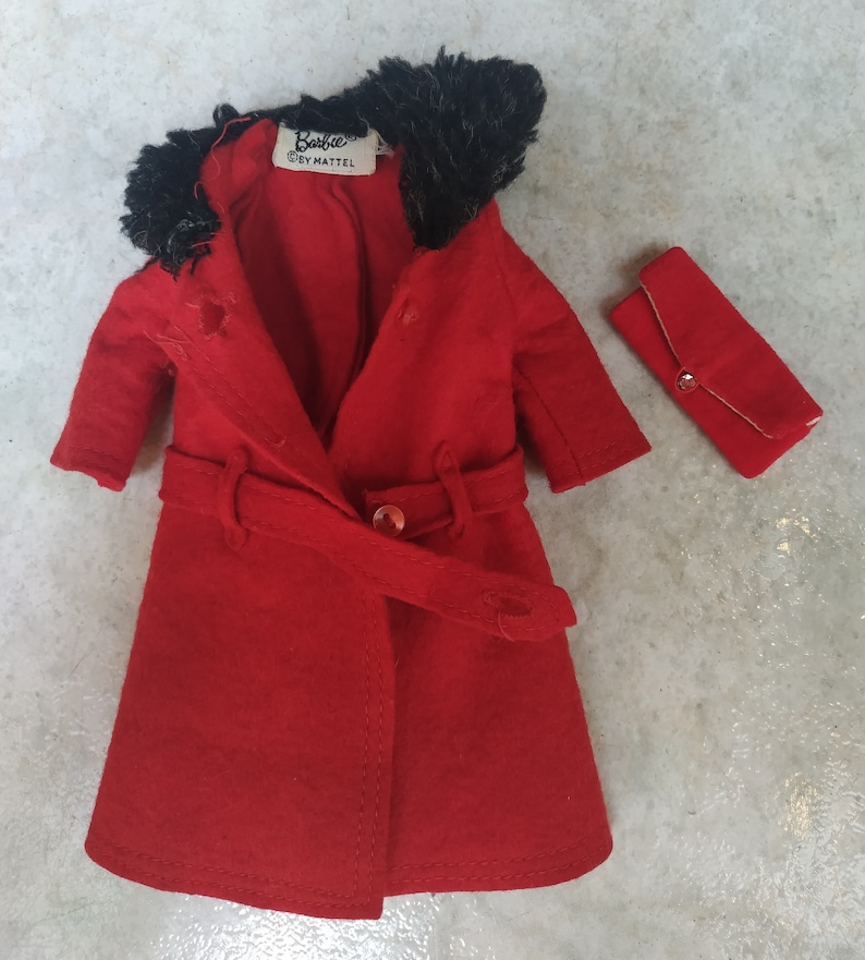 May include: A red coat with a black fur collar and a matching red clutch. The coat has a belt and a button closure. The label on the coat reads "Barbie by Mattel."