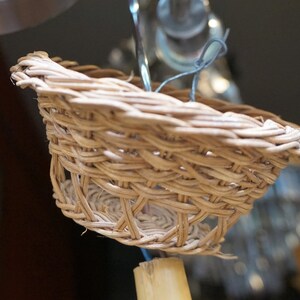 May include: A close-up of a small, woven basket made of natural materials. The basket is light brown and has a round shape. It is hanging from a wire.