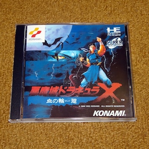 May include: A CD case for the Super CD-ROM² game "Vampire Killer: Rondo of Blood" for the PC Engine. The case features a red and black background with a character holding a whip and a bat flying in the background. The text on the case reads "Vampire Killer: Rondo of Blood" in Japanese and "KONAMI" in English.
