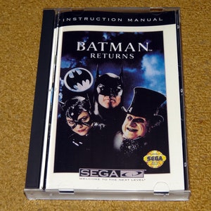 May include: Instruction manual for the Sega Genesis video game Batman Returns. The cover features a dark blue background with images of Batman, Catwoman, and the Penguin. The text "Batman Returns" is in white with a red outline. The Sega logo is in the bottom right corner.