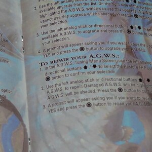 May include: A page from a video game instruction manual with a blue and white background. The text explains how to repair and upgrade the A.G.W.S. using the left analogue stick or directional buttons. The text also includes the button symbols for confirming selections.