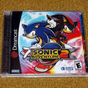 May include: A Sonic Adventure 2 video game case for the Dreamcast. The cover art features Sonic the Hedgehog and Shadow the Hedgehog. The game case is in a clear plastic case with the Dreamcast logo on the side.