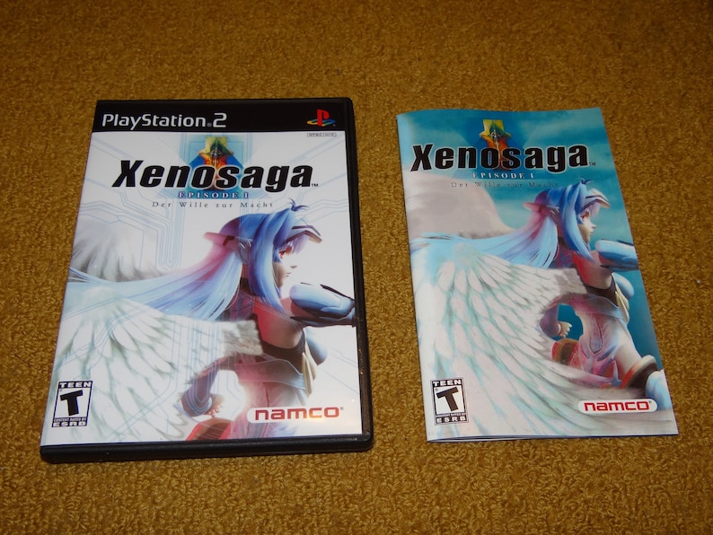 May include: A PlayStation 2 video game case and instruction manual for Xenosaga Episode I: Der Wille zur Macht. The case features a blue and white image of a woman with wings. The manual has a similar image.