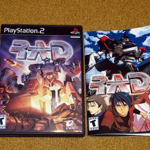 May include: A PlayStation 2 video game case and manual for the game "3D Robot Alchemic Drive." The case features a large robot illustration with a cityscape background. The manual shows anime characters and a robot.