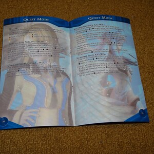 May include: A two-page spread from a video game instruction manual. The left page shows a character from the game, a woman with long blue hair, wearing a blue and white outfit. The right page shows the text "QUEST MODE" and instructions for upgrading and repairing a character's A.G.W.S. in the game.