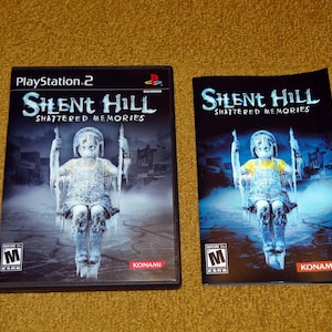 May include: A PlayStation 2 video game case and instruction manual for Silent Hill: Shattered Memories. The cover art features a young girl in a white dress standing on a swing set. The game is rated M for Mature by the ESRB.