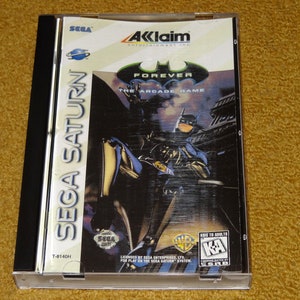 May include: A Sega Saturn video game case for Batman Forever: The Arcade Game. The case is black with a clear plastic front. The front of the case features a picture of Batman in his suit, standing in front of a cityscape. The game is rated "K-A" for Kids to Adults.