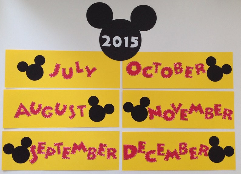 May include: A set of six yellow cards with red Mickey Mouse-shaped letters spelling out the months of July, August, September, October, November, and December. Each card has a black Mickey Mouse head on the side. The top card has a black Mickey Mouse head with the year 2015 in white text.