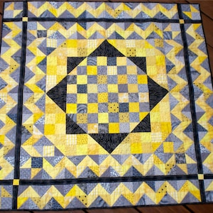 May include: A quilt with a black, gray, and yellow geometric pattern. The quilt is made up of squares and triangles. The quilt is bordered with a black and gray trim.