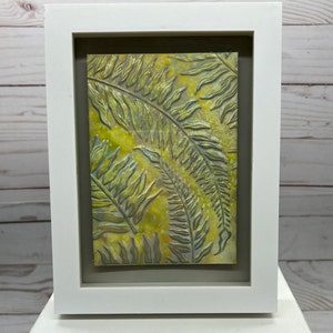 May include: A framed artwork featuring a textured, embossed design of fern leaves in shades of green and yellow.