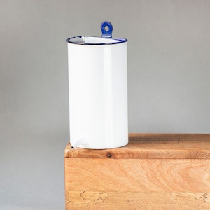 May include: A white enamel jug with a blue rim and handle sits on top of a wooden box with a natural wood grain finish. The box has a carved design on the front.