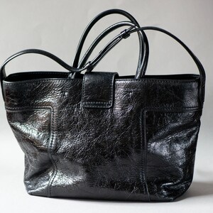 Un sac cabas Tod's en cuir noir avec fermeture à boucle argentée. Ce sac en cuir texturé est doté d'une bandoulière longue. Il présente un fermoir à boucle orné du logo Double T ton sur ton sur la languette avant. Une bandoulière plate et longue en cuir est également fournie pour un porté épaule polyvalent.
