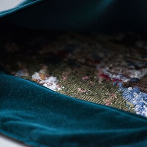 May include: A teal velvet pouch with a colorful woven fabric lining. The pouch is open and the lining is visible.