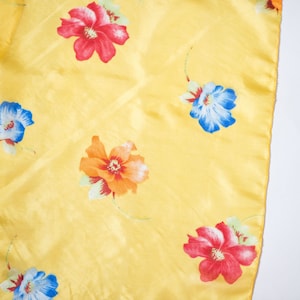 May include: A yellow fabric with a floral pattern. The flowers are red, blue, and orange.