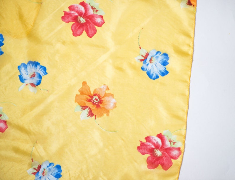 May include: A yellow fabric with a floral pattern. The flowers are red, blue, and orange.